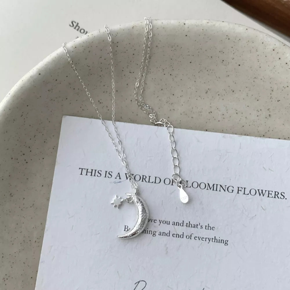 Sterling silver necklace with crescent moon and star charm, adjustable chain.