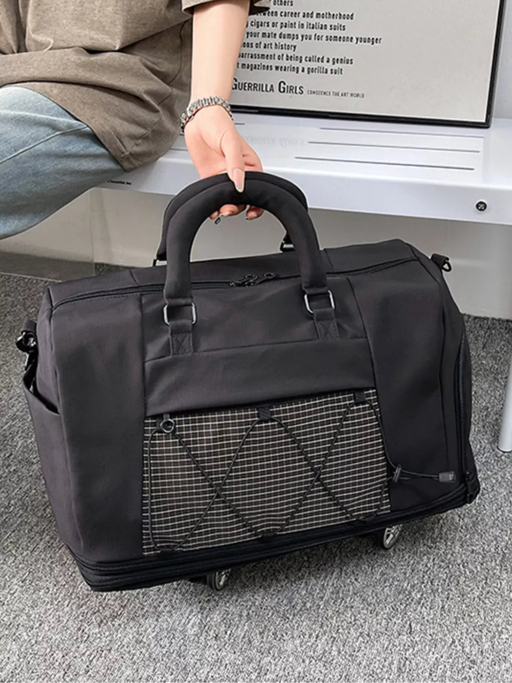 Black rolling travel organizer bag with a checkered front pocket and elastic cord detail.