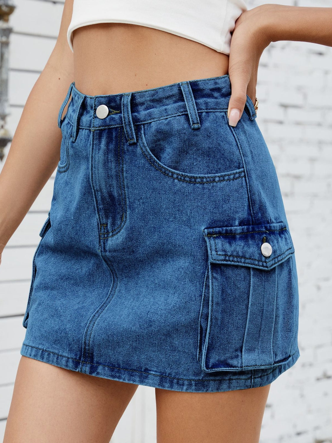 Denim cargo mini skirt in medium blue with button closure and pleated flap pockets.