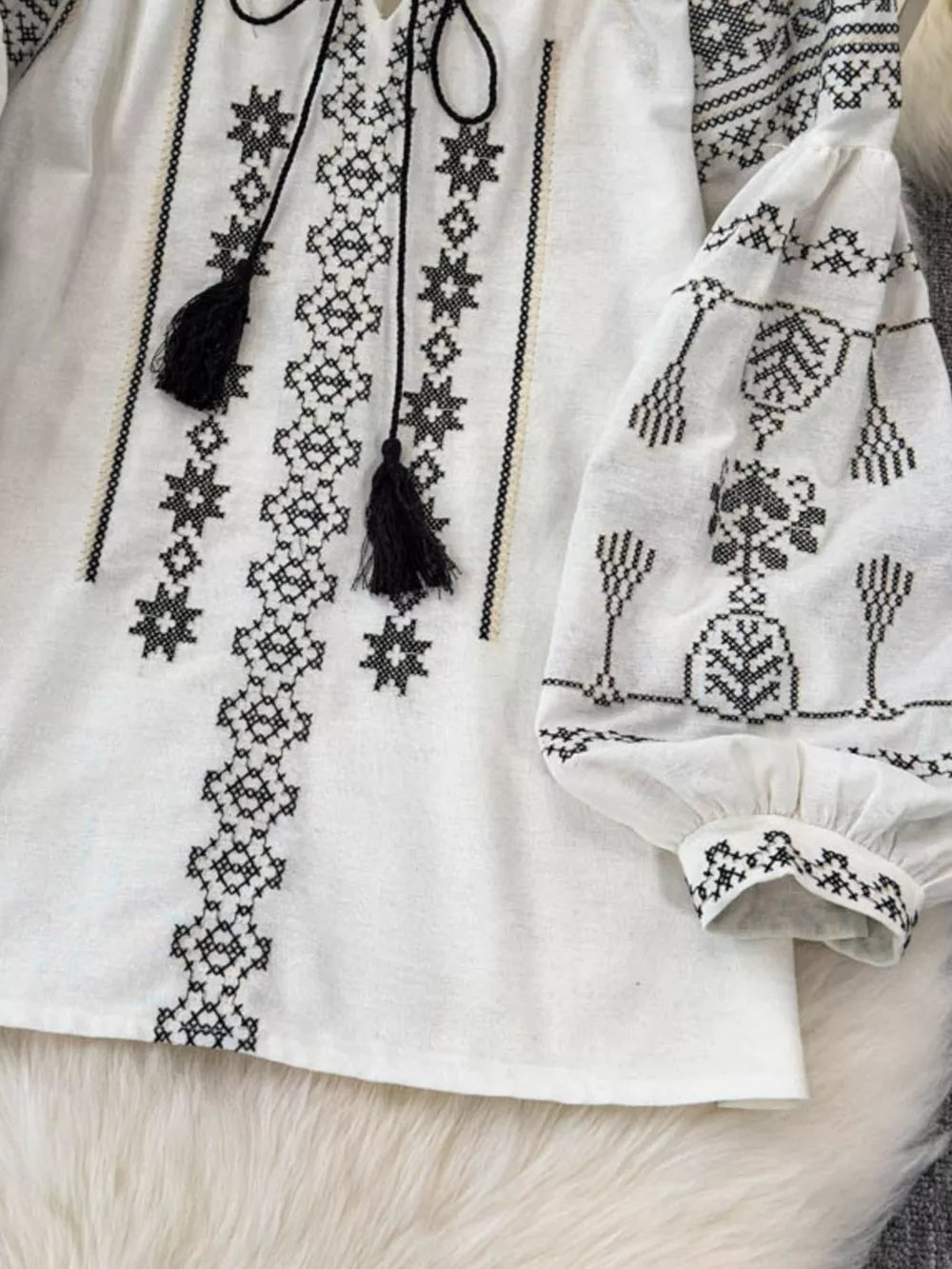 White embroidered tie neck blouse with black tassels and puff sleeves.