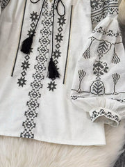 White embroidered tie neck blouse with black tassels and puff sleeves.