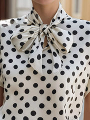 White polka dot shirt with a large black bow tie neck and cap sleeves.