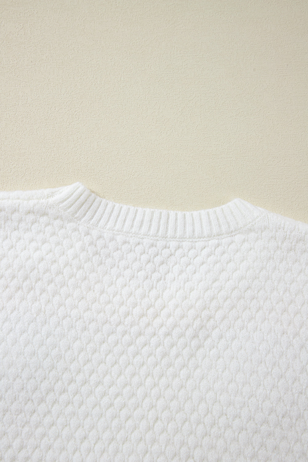 White knit sweater with textured diamond pattern and ribbed crew neck.