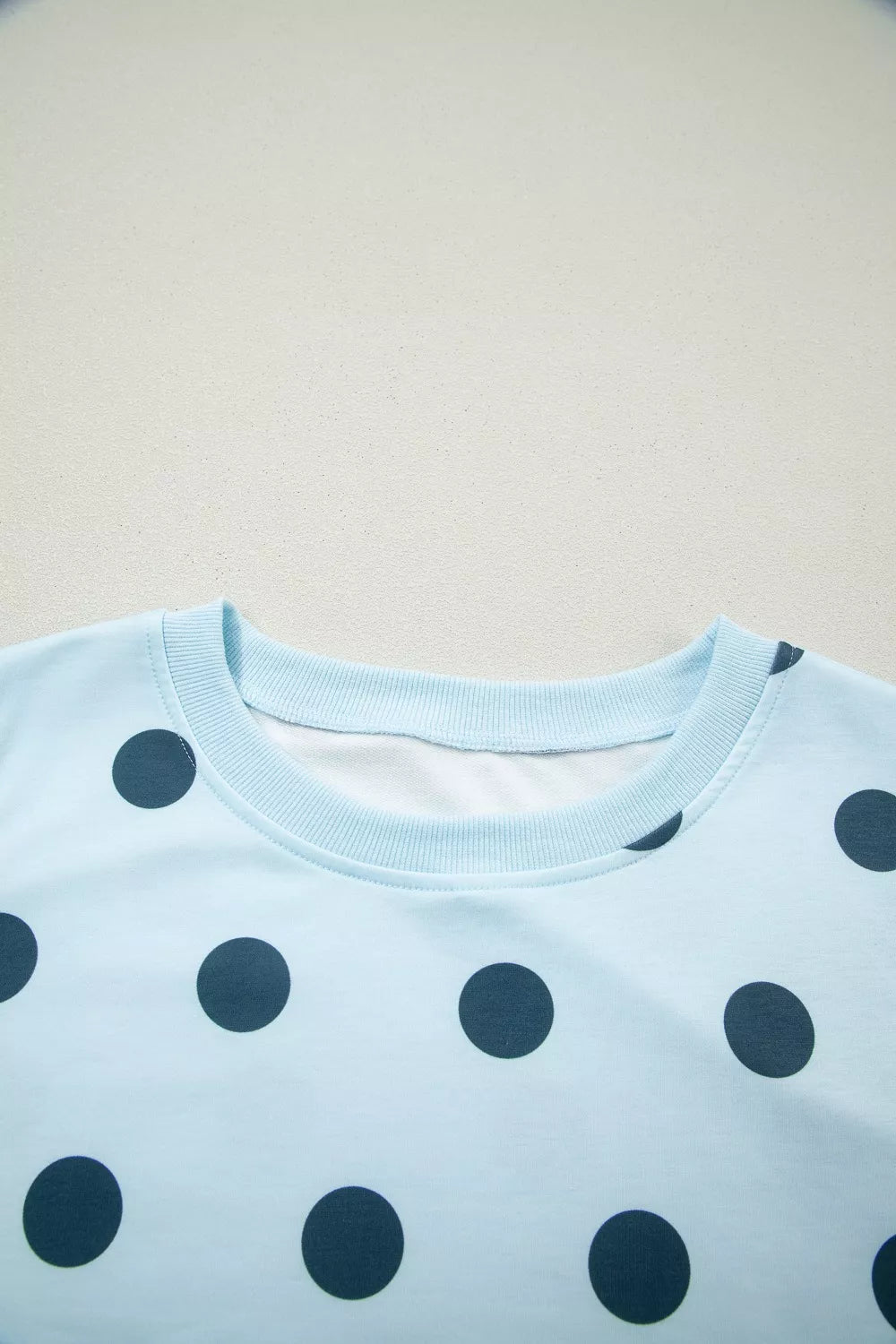 Pastel blue polka dot crew neck top with ribbed collar and cuffs.