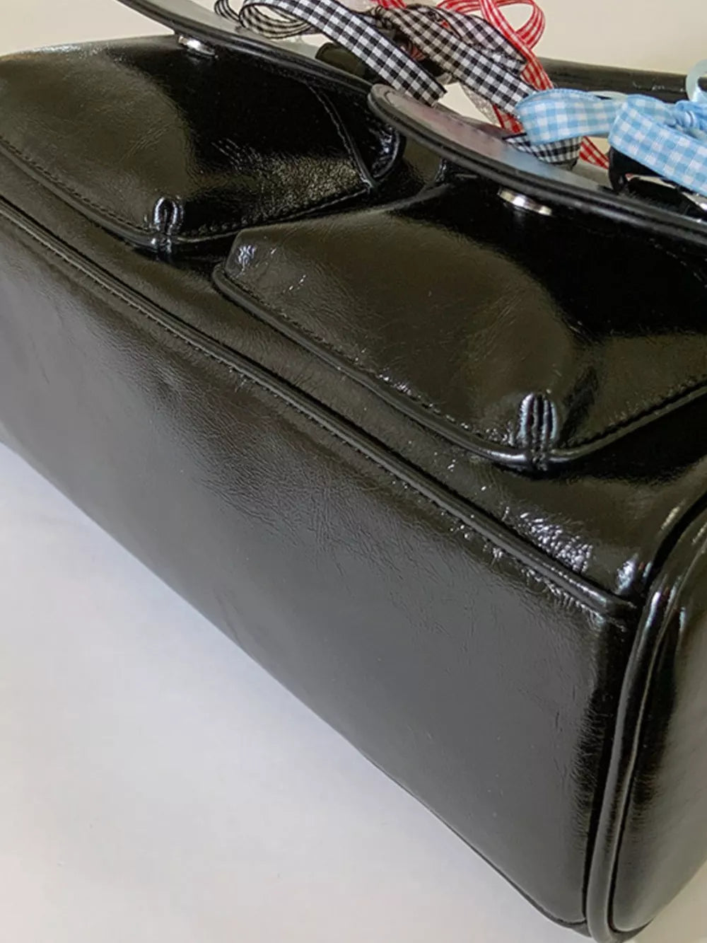 Black patent shoulder bag with ribbon embellishments and front flap pockets.