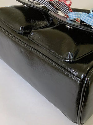 Black patent shoulder bag with ribbon embellishments and front flap pockets.