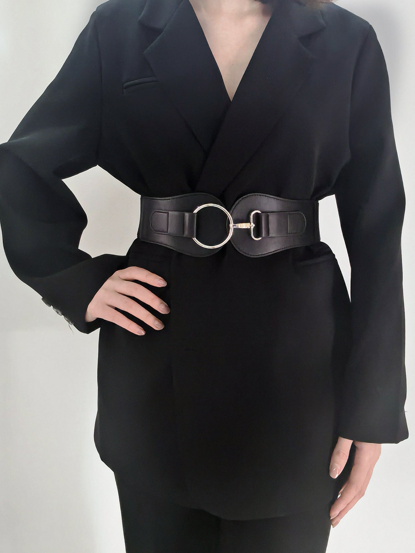 Black cincher belt with silver buckle detail worn over a blazer.