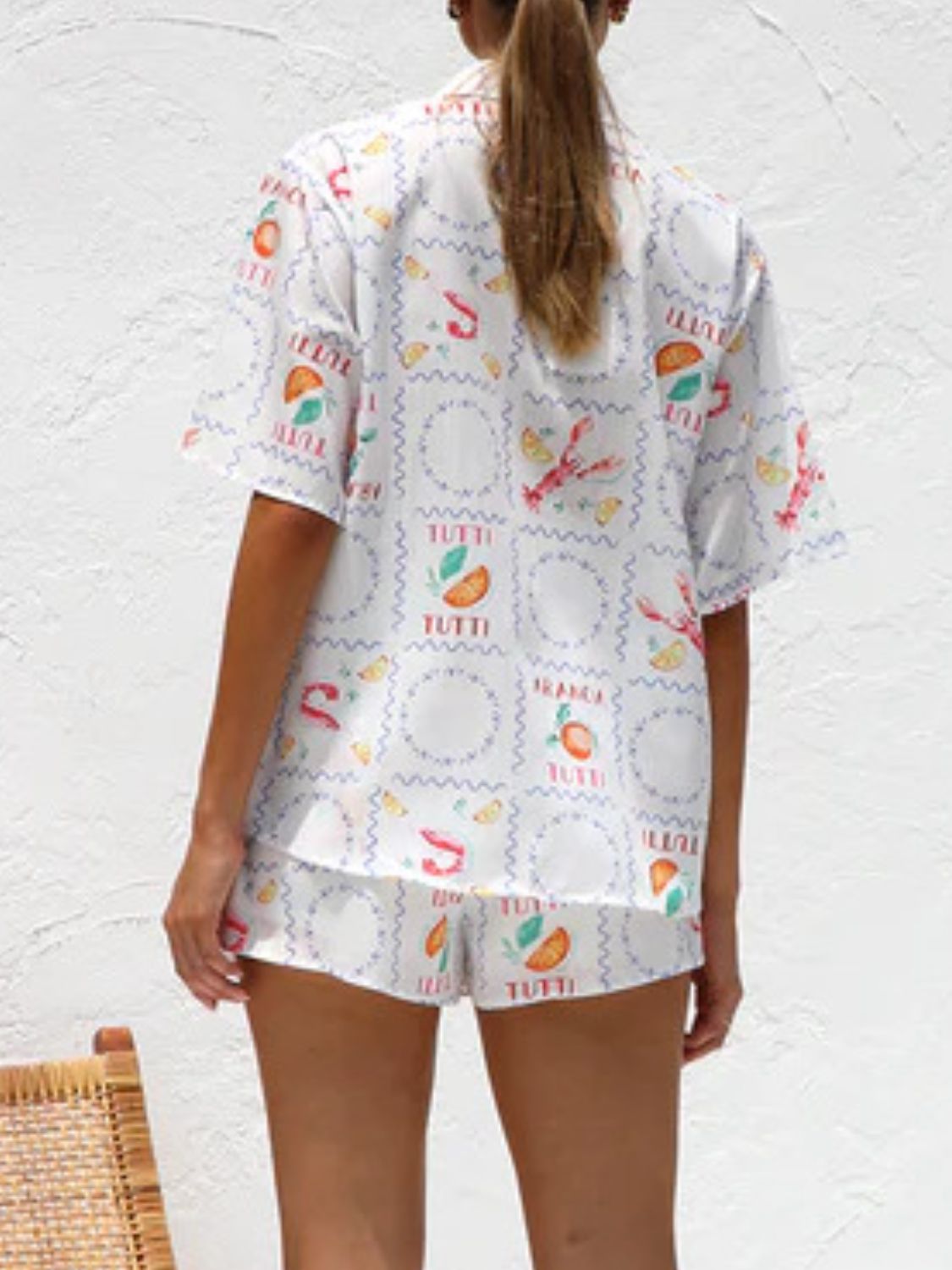 White resort set with citrus and lobster print, featuring a button-up shirt and shorts.