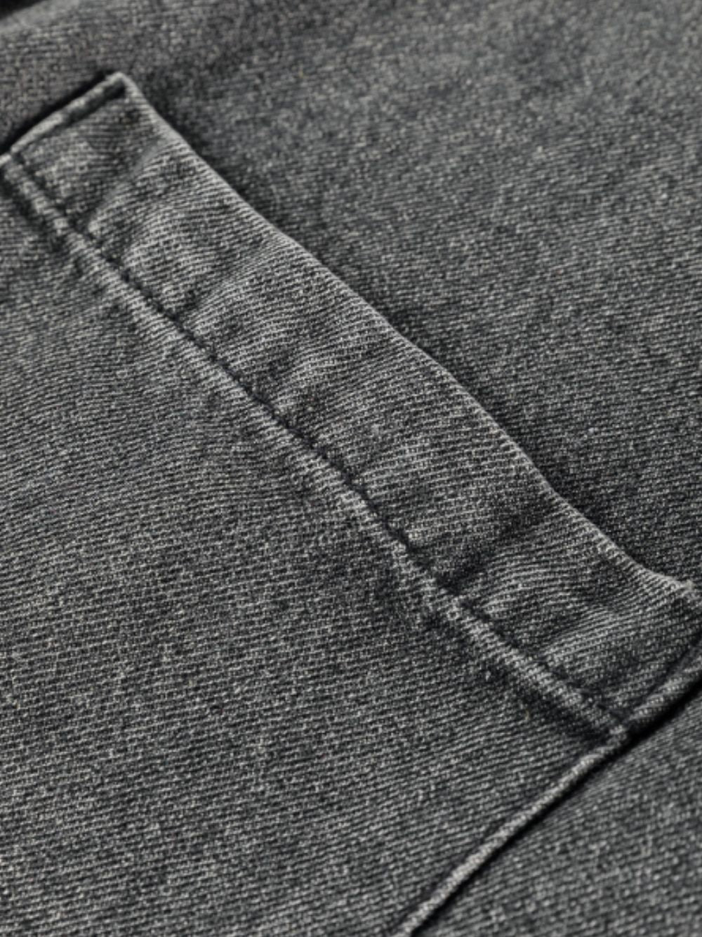 Faded gray denim pinafore dress detail showing a pocket with visible stitching.