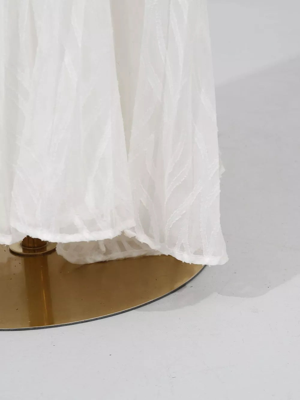 White maxi dress with textured leaf pattern and balloon sleeves, shown on a gold stand.