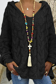 Black cable knit hooded cocoon sweater with V-neck and tassel necklace.