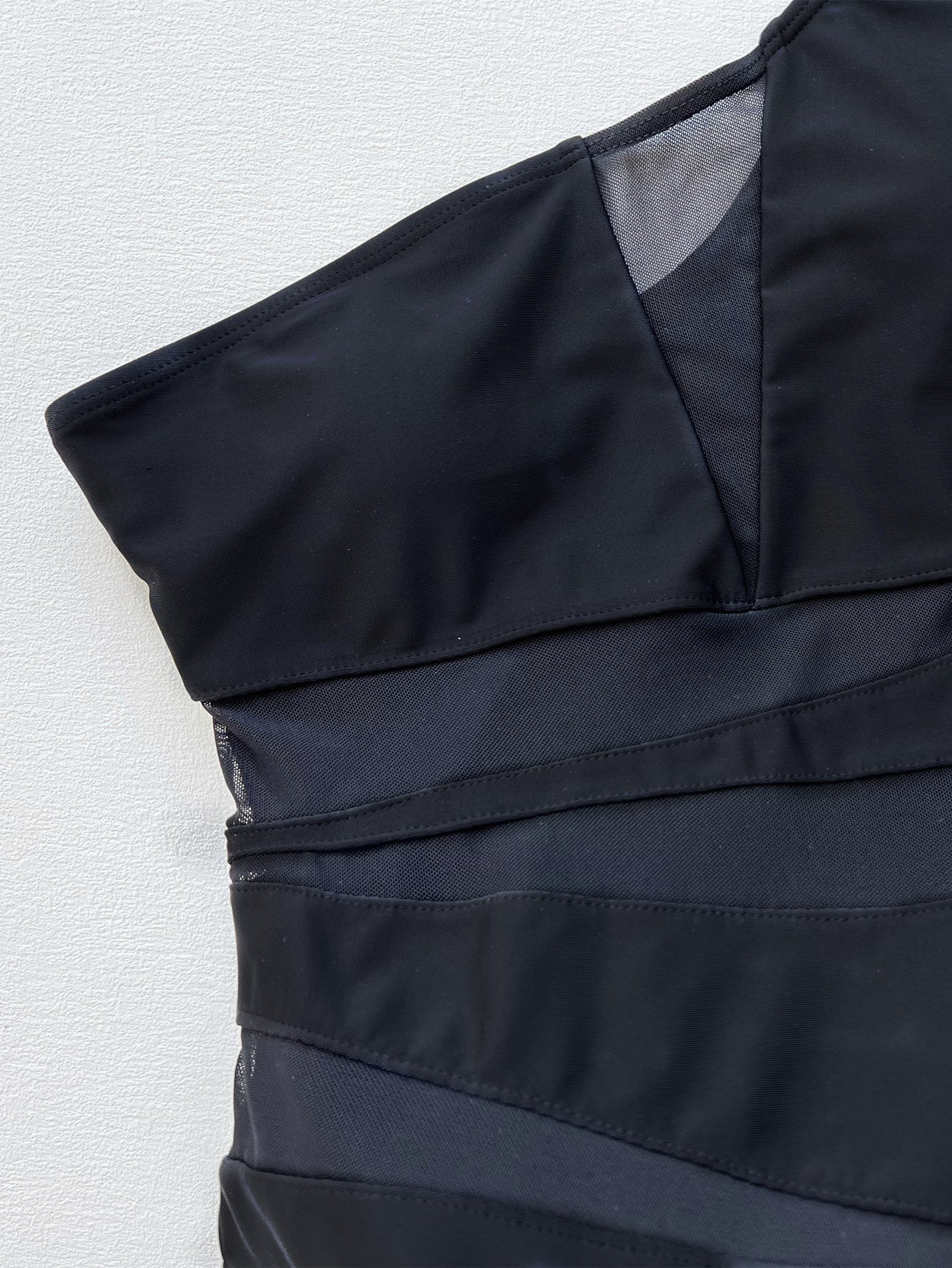 Black asymmetrical one-piece swimsuit with mesh panels and strap details.