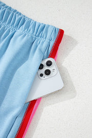 Light blue activewear shorts with rainbow stripe detail and elastic waistband, showing pocket detail.