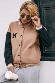 Camel bomber jacket with black sleeves and an M patch, featuring snap buttons and striped trim.