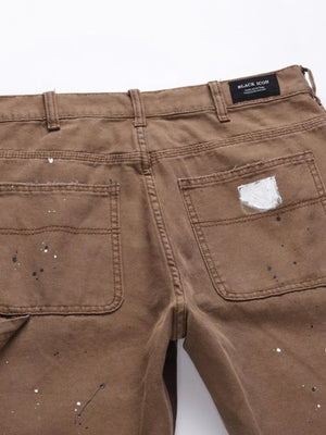Taupe carpenter trousers with artisan paint splatters and distressed details.
