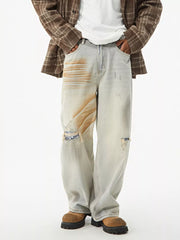 Distressed light wash wide-leg jeans with unique tan paint splatters and ripped knee details.