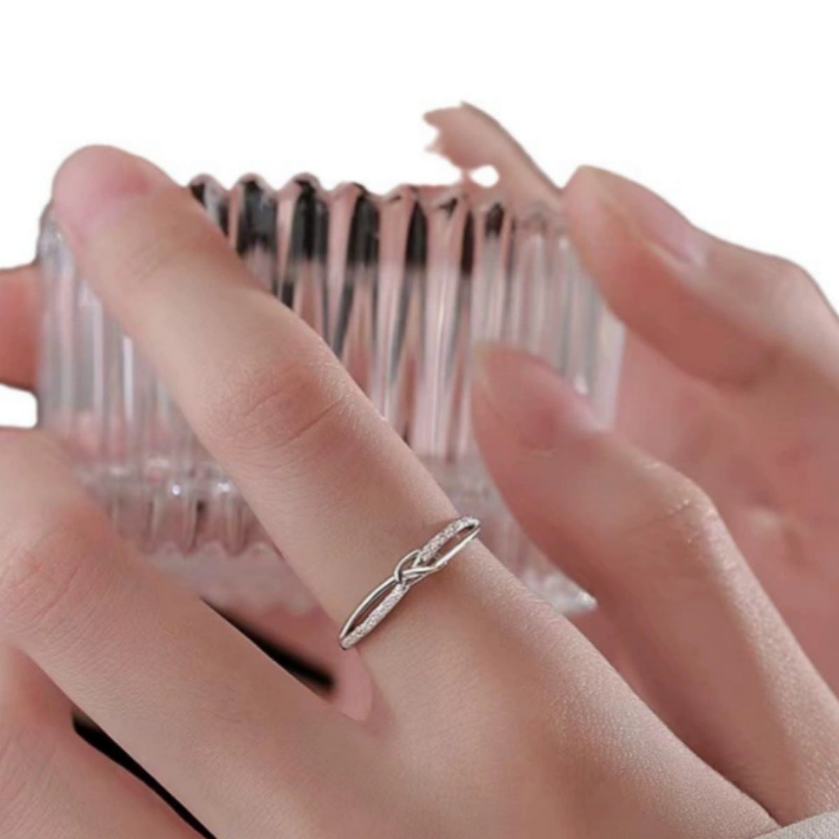 Silver knot ring with pave detail on a finger, showing adjustable band.