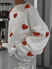 White oversized knit crewneck sweater with all-over red heart pattern and drop sleeves.