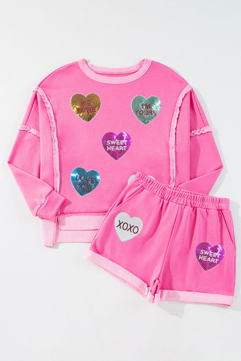 Pink loungewear set with sequin heart appliques and text details.