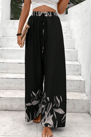 Black wide-leg lounge trousers with botanical print hem and drawstring waist.