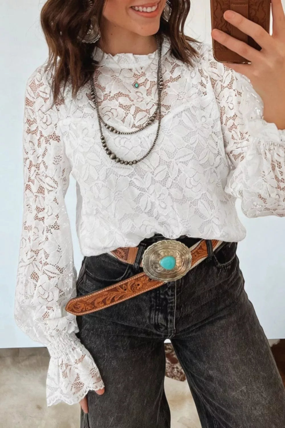 White lace blouse with ruffled neckline and bell sleeves, styled with a turquoise concho belt.