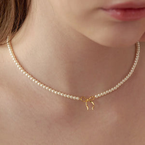 Delicate pearl choker necklace with a gold bow pendant.