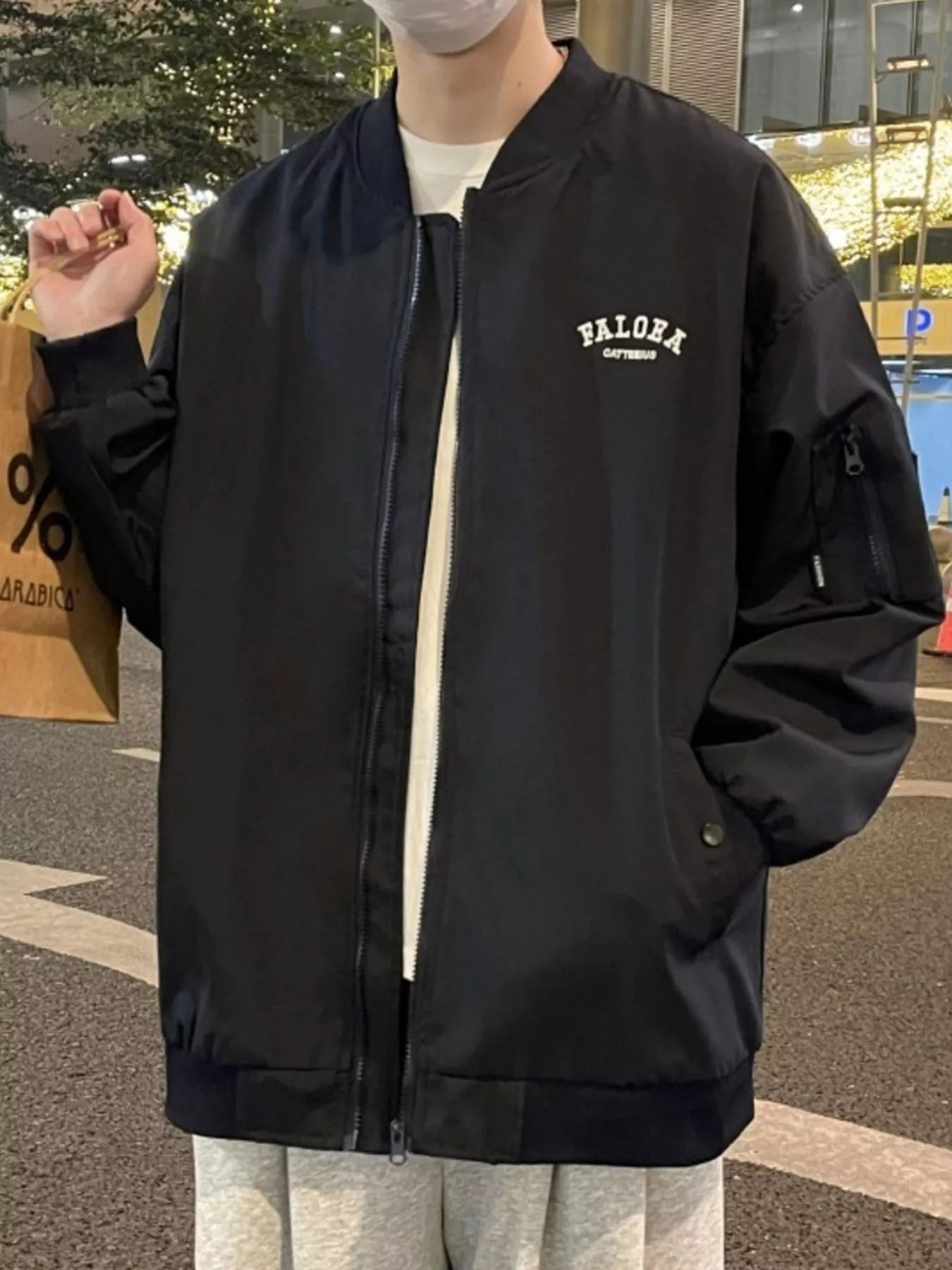 Black bomber jacket with white chest logo, zip front, and utility sleeve pocket.