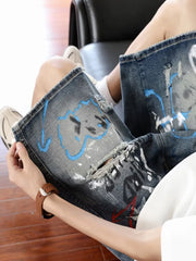 Men's distressed denim shorts with graffiti-style paint splatters and rips.
