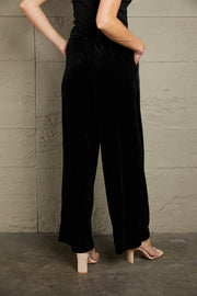 Black velvet palazzo trousers with a high waist and wide leg, shown from the back.