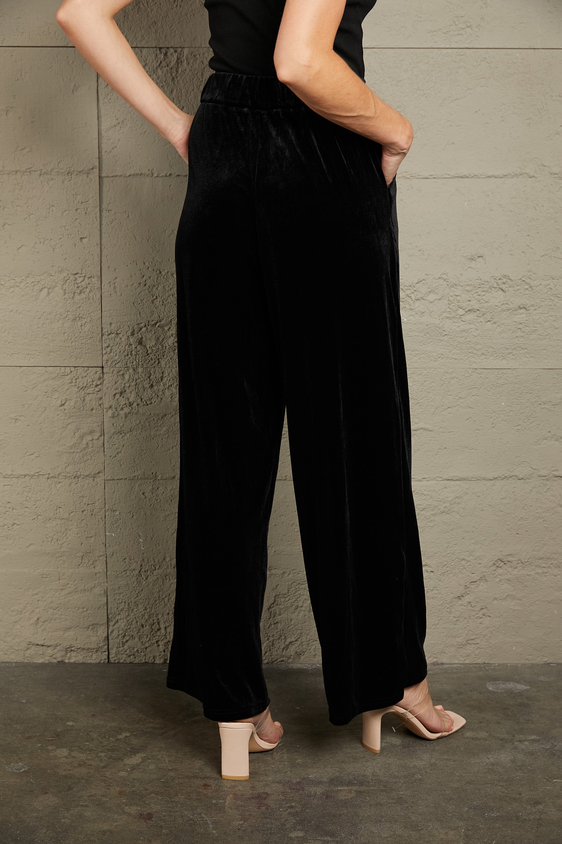 Black velvet palazzo trousers with a high waist and wide leg, shown from the back.