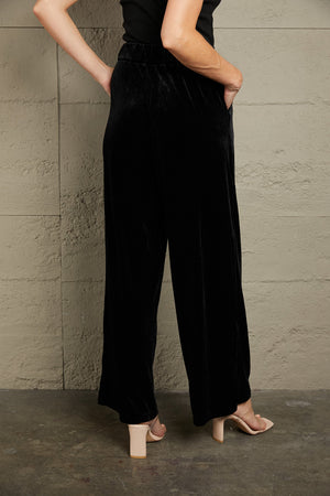 Black velvet palazzo trousers with a high waist and wide leg, shown from the back.