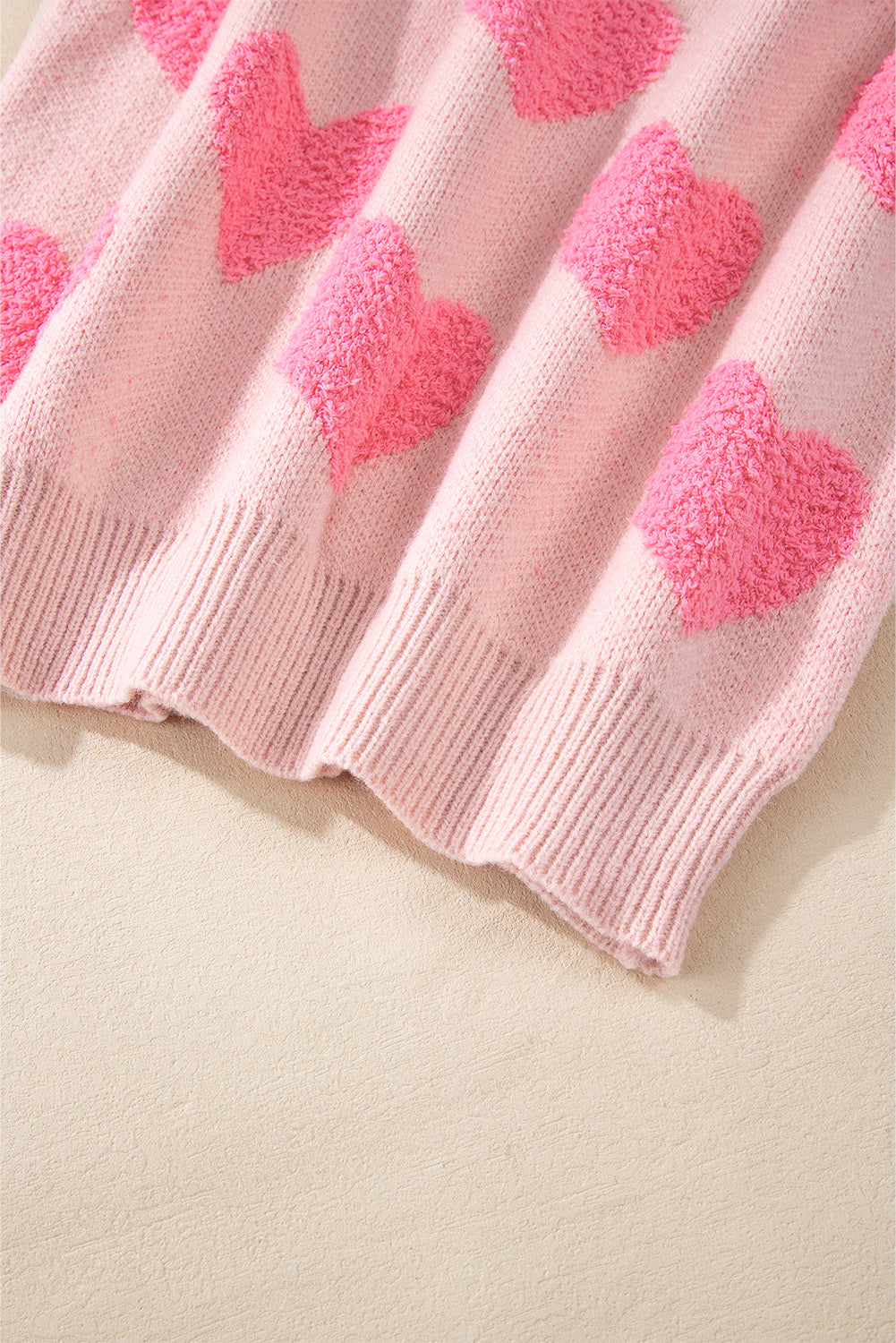 Blush pink knit sweater with textured heart motif and ribbed hem.