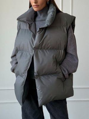 Dark gray padded puffer vest with a high collar and zip front, worn over a gray turtleneck.