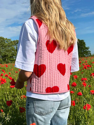 Quilted blush pink vest with red heart appliqué, featuring a tie closure and crew neck.