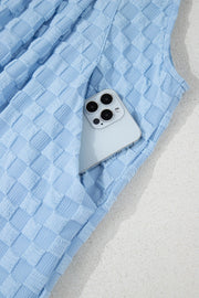 Light blue textured checkered palazzo jumpsuit with a phone in the pocket.