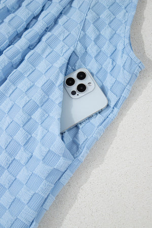 Light blue textured checkered palazzo jumpsuit with a phone in the pocket.