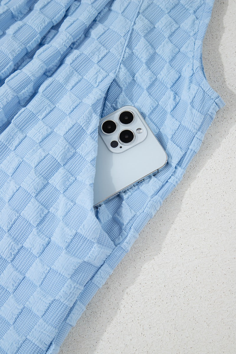 Light blue textured checkered palazzo jumpsuit with a phone in the pocket.