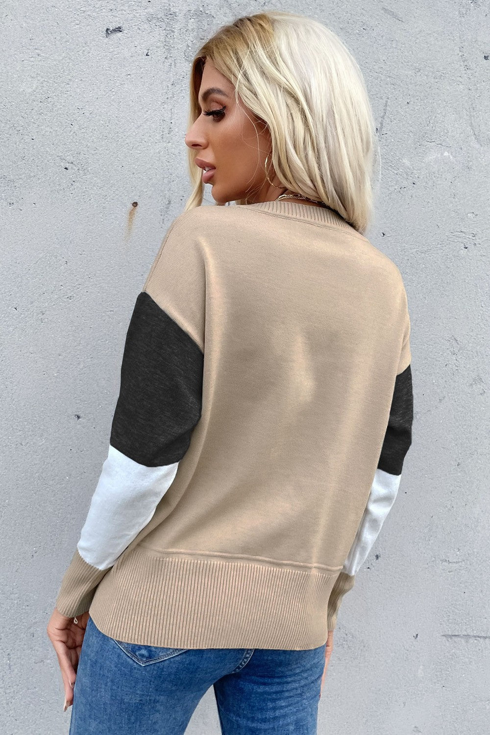 Geometric panel knit sweater in tan with black and white sleeves, crew neck, and ribbed hem.