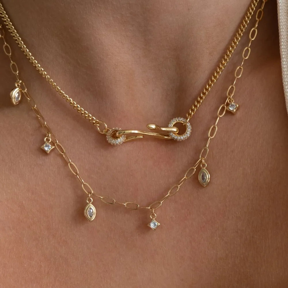 Gold curb chain necklace with pave CZ clasp and dangling charms, layered with a delicate chain necklace.