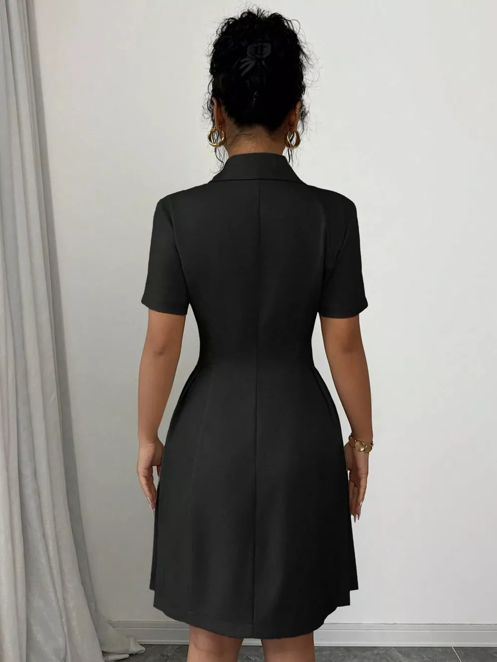 Black double-breasted pleated blazer dress with short sleeves and a collared neckline.