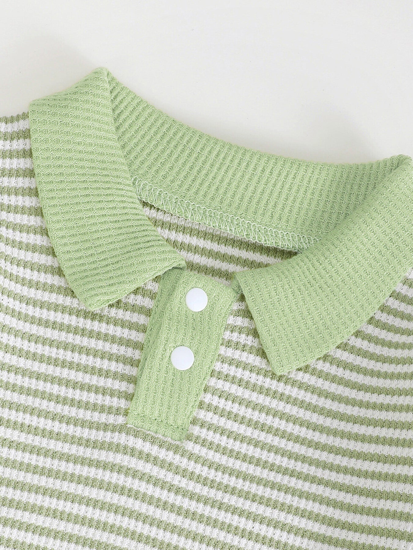 Green and white striped polo shirt with waffle knit texture and two white buttons.