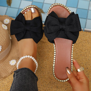 Black bowknot sandals with gold trim, styled with a pearl anklet.
