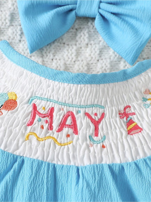 Embroidered May birthday motif white cotton baby one-piece with blue trim and bow.