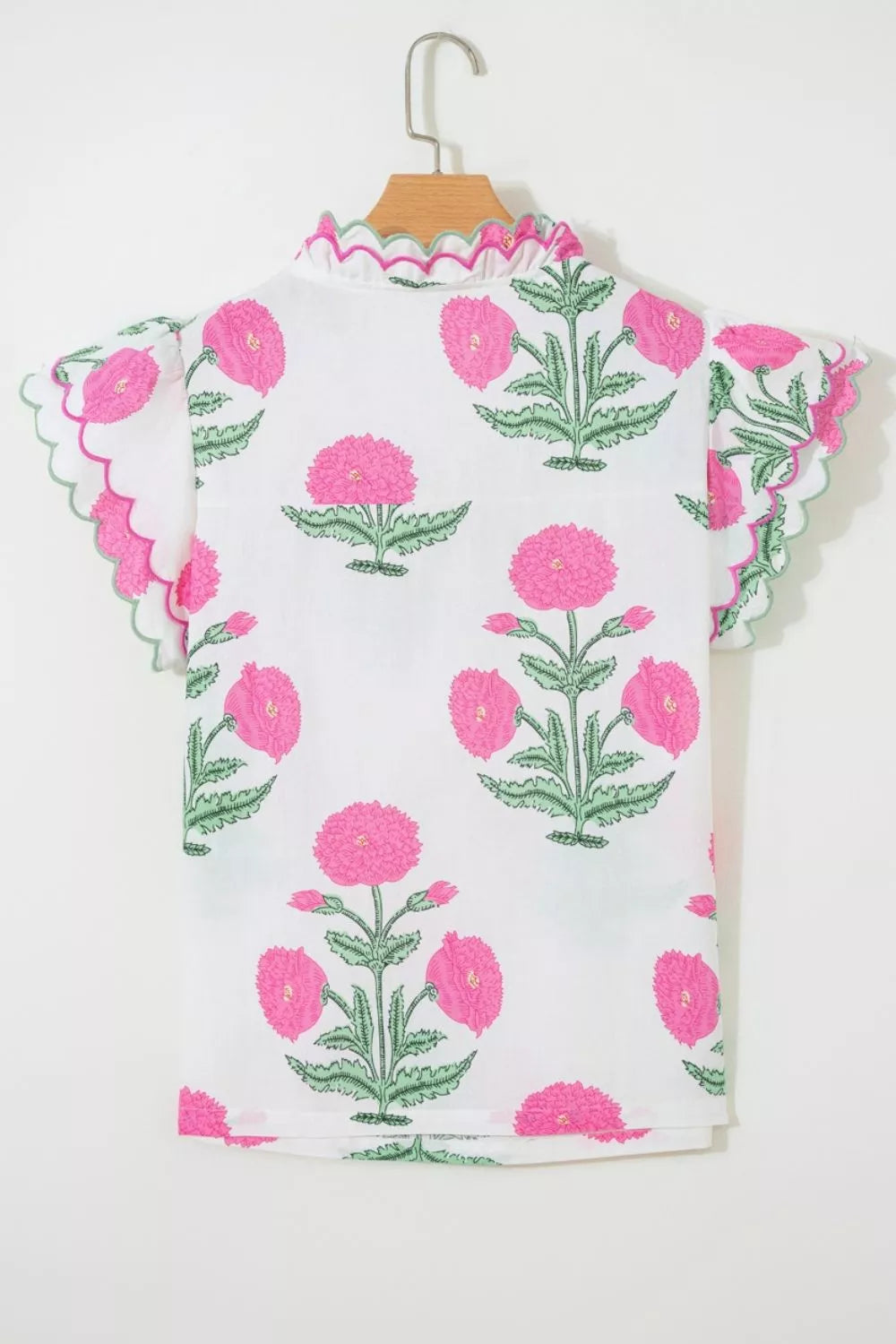 White cotton blouse with pink floral print, ruffled neckline and scalloped sleeves.