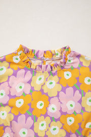 Puff sleeve blouse with ruffle trim and a bold floral print in purple, yellow, pink, and green.