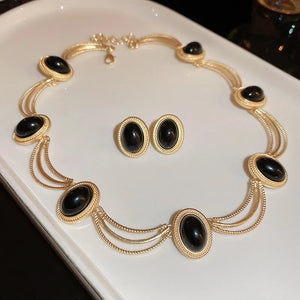 Gold oval stone stud earrings and matching necklace with black gemstones.