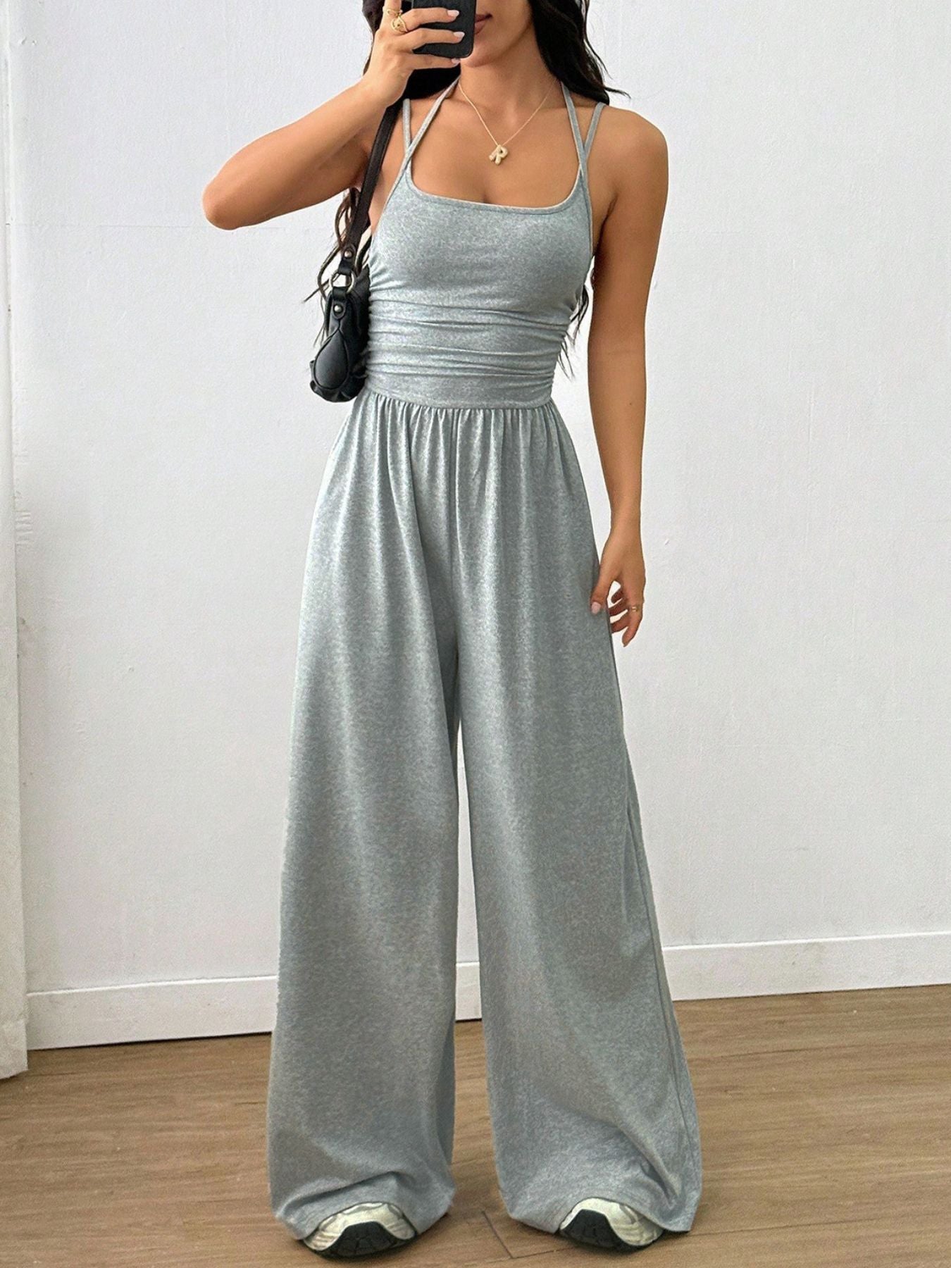 Gray wide-leg jumpsuit with ruched waist and halter neck, styled with sneakers.