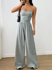 Gray wide-leg jumpsuit with ruched waist and halter neck, styled with sneakers.