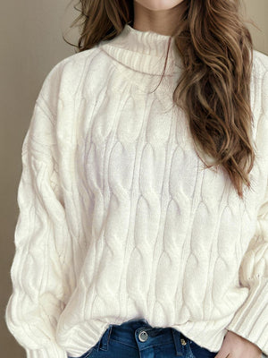 Ivory oversized cable knit turtleneck sweater with prominent cable detailing.