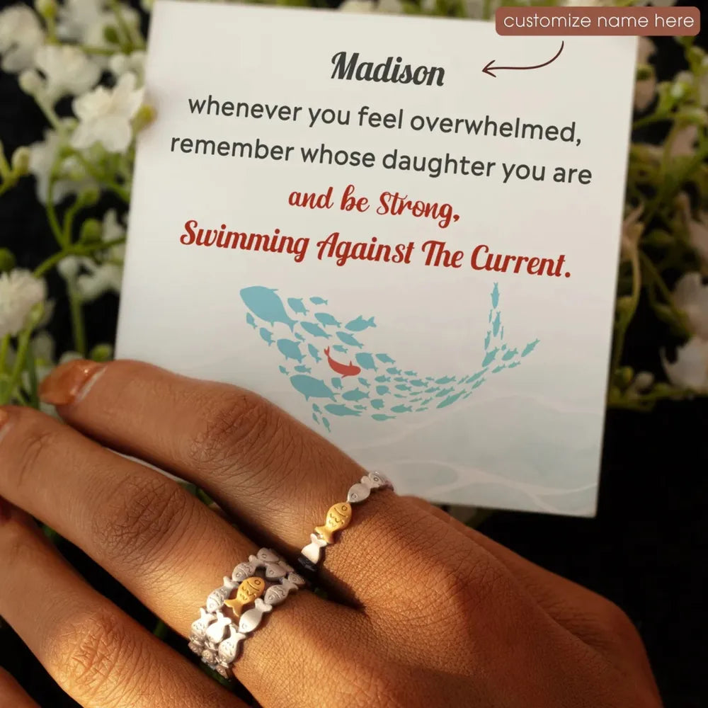 Adjustable rings with fish motifs, one gold, one silver, on a hand with a card.